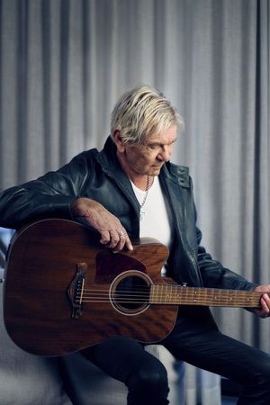 Matthias Reim sitzt mit einer Gitarre vor einem Vorhang.