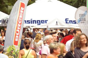 Menschen stehen an den Gastronomiehütten der BÜRGER Freilichtbühne unter großen Sonnenschirmen