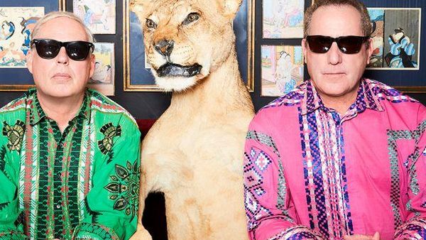 Die beiden Musiker von OMD schauen mit aufgesetzten Sonnenbrillen in die Kamera. Zwischen ihnen sitzt eine Löwin.
